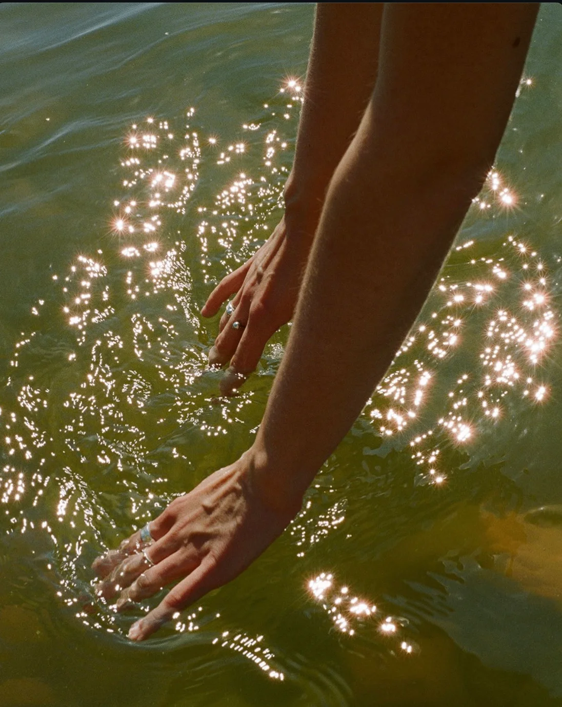 Two hands reaching into sunlit water